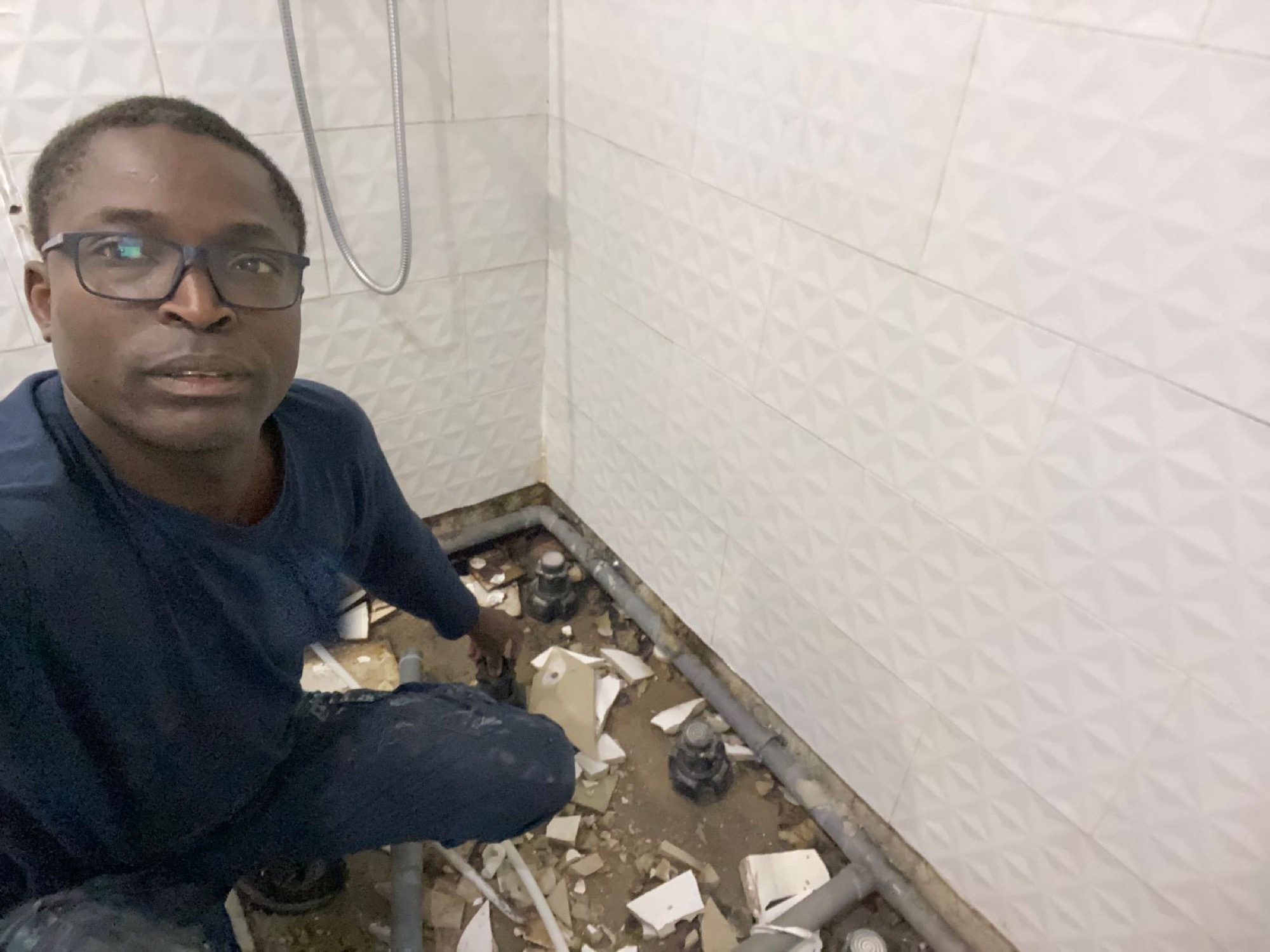 Christian Niangouna agenouillé dans une salle d'eau en intervention, dépose du receveur et reprise des évacuations