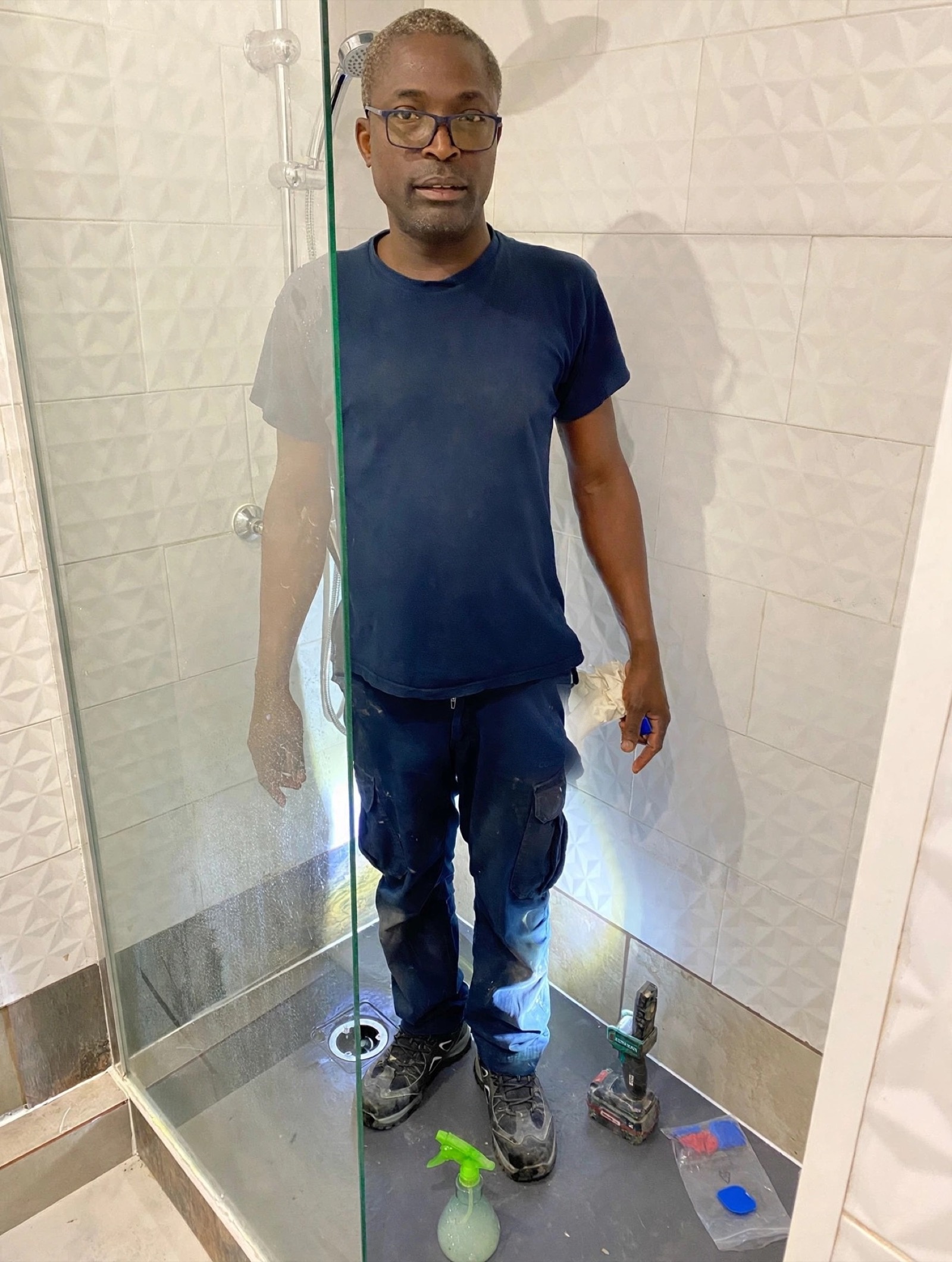 Christian Niangouna en tenue de travail dans une douche à l'italienne en cours de finition, outils posés au sol